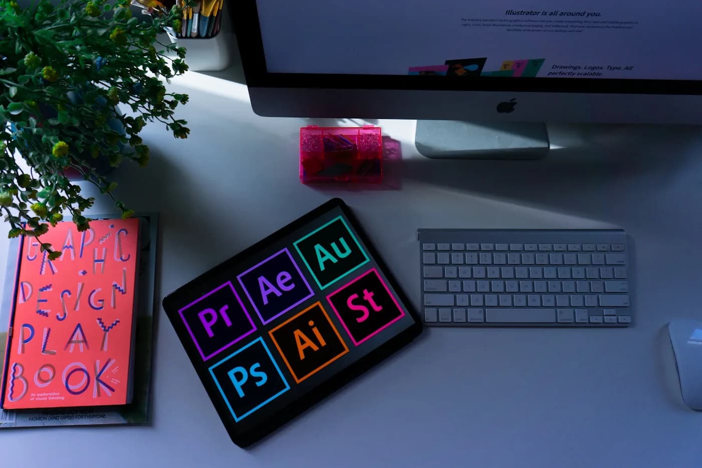 Designer's desk with an iMac, tablet showing design software, and a graphic design playbook