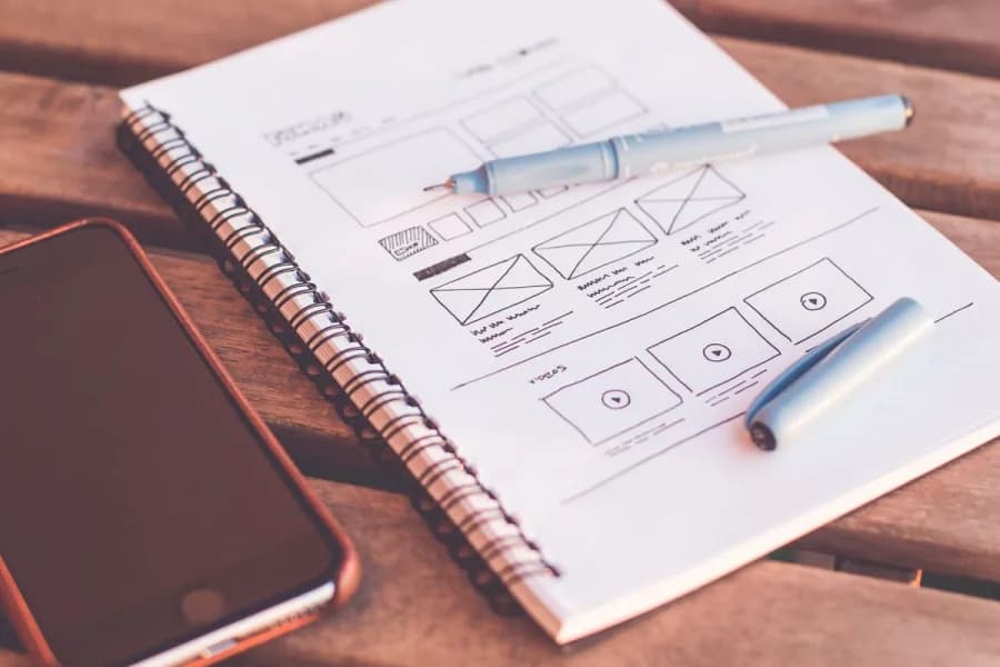 Hand-drawn website wireframe sketch in a spiral notebook next to a phone